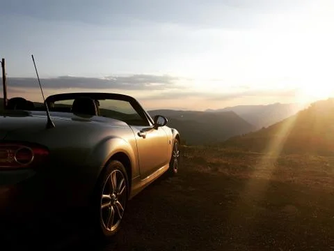 Sunset back view of silver gray convertible car, mountain valley in background Stock Photos