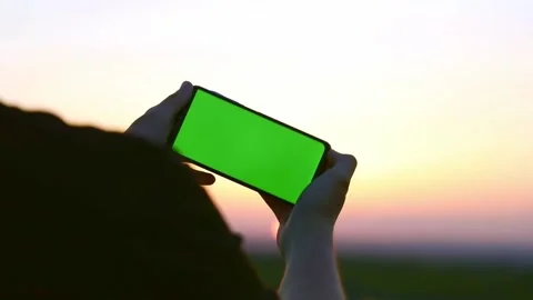 On a sunset background, hands with a phone with a green screen Stock Footage 193968799
