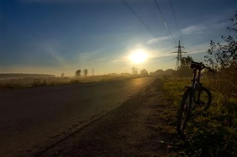 Sunset in background of the road and fields with grass and trees Stock Photos
