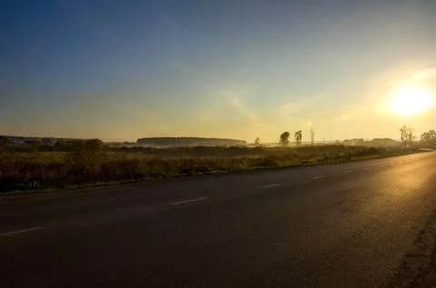 Sunset in background of the road and fields with grass and trees Stock Photos