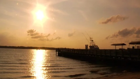 Sunset by beach with a boat docked at oceanfront pier Stock Footage 117249491