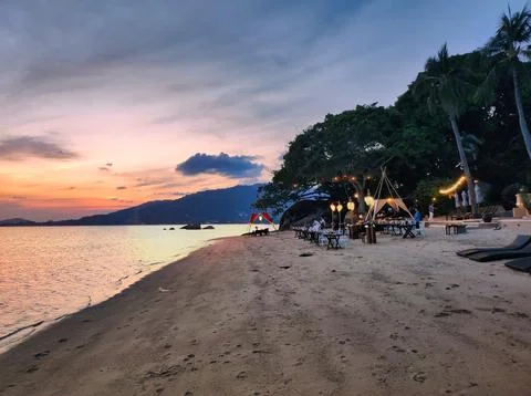 Sunset at a beach with dining tables and tents set up for evening gathering.. Stock Photos