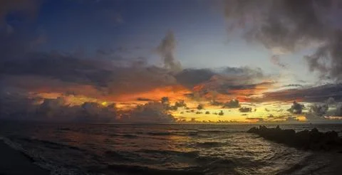 Sunset on the beach with a dramatic sky with clouds and an orange hue Stock Photos