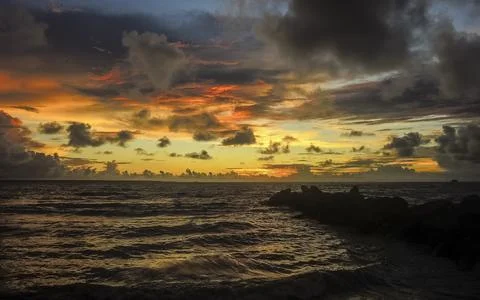 Sunset on the beach with a dramatic sky with clouds and an orange hue Stock Photos