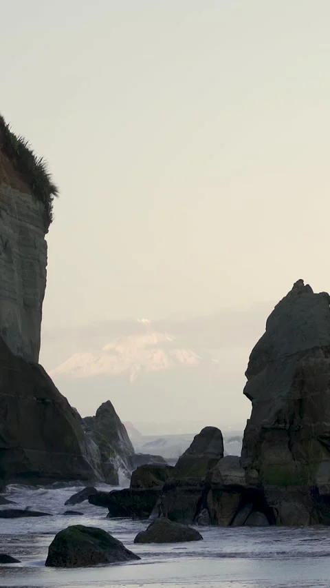 Sunset by beach full of rock formations and snowy peak mountain behind. Thr.. Stock Footage 289103563
