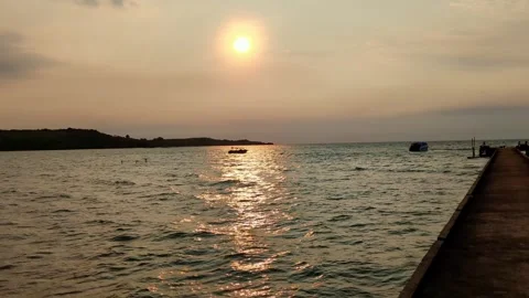 Sunset at the beach with a pier over the ocean reflecting in the water Stock Footage 276602272