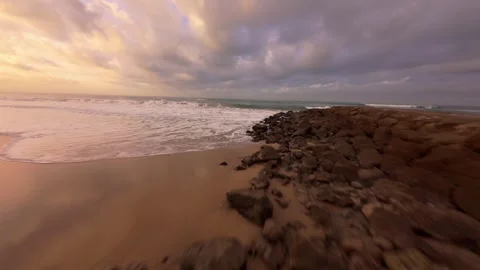 Sunset beach scene with foamy waves, sandy shore, and distant resort buildings Stock Footage 344542893
