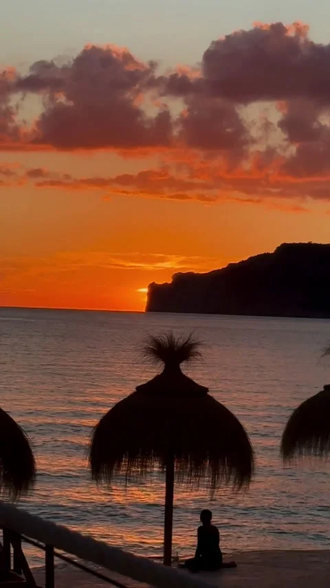 Sunset beach scene with straw umbrellas, people silhouettes and glowing horizon Video stock 318075622