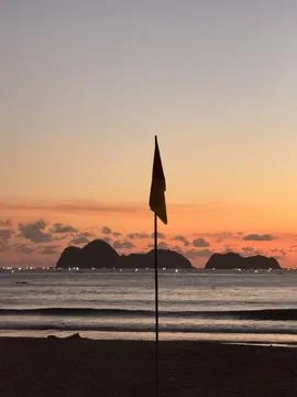 Sunset Beach with Silhouetted Flag and Distant Islands. Pulau Merah Beach B.. Stock Photos