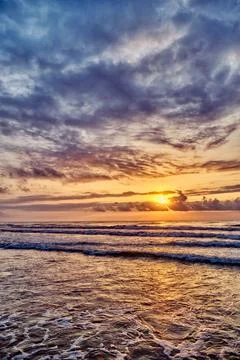 Sunset at the beach with waves and clouds over the ocean horizon in the eveni Stock Photos
