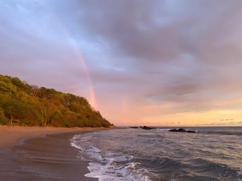 Sunset at the beach with waves and rainbow in the sky Stock Photos