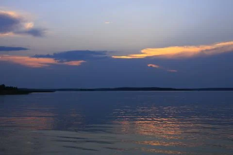 Sunset behind the blue clouds above the quiet lake water Stock Photos