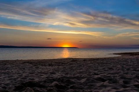Sunset behind a distant cape, view from a deserted sandy shore Stock Photos