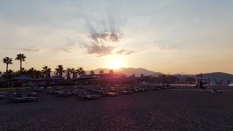 Sunset behind the mountain on the beach with sun loungers and umbrellas on Video stock 303621486
