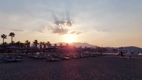 Sunset behind the mountain on the beach with sun loungers and umbrellas on Stock-Footage 304959873