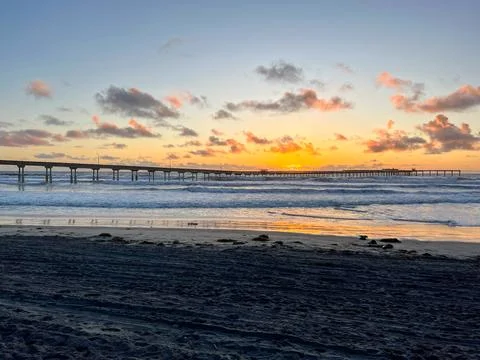 Sunset behind ocean beach pier with crashing waves Stock Photos