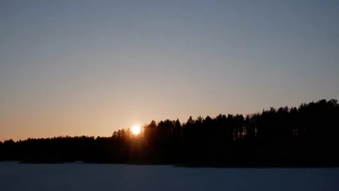Sunset behind a winter forest on the shore of a snow-covered lake. Timelapse. Stock Footage 178590809