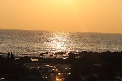 Sunset casting orange reflections across the sky and the ocean water Stock Photos