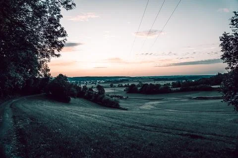 A sunset casting vibrant colors over a field with trees nearby Stock Photos