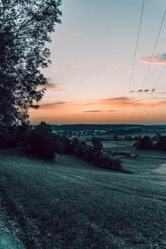 A sunset casting vibrant colors over a field with trees nearby Stock Photos