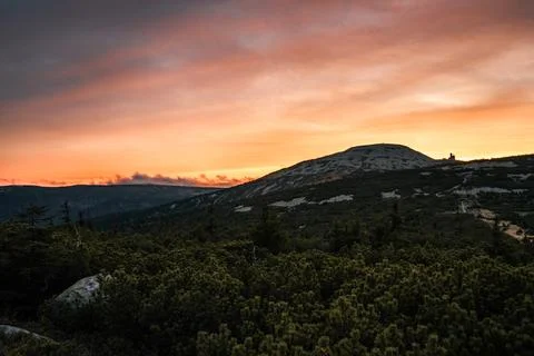 A sunset casting vibrant colors over mountains and lush trees Stock Photos