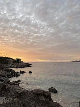 Sunset casting a warm afterglow over lake with rocky shore, under a cloudy sky Stock Photos