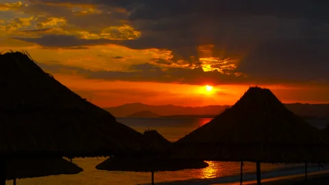 Sunset casting a warm glow behind beach umbrellas on a tranquil evening Stock Footage 300807139