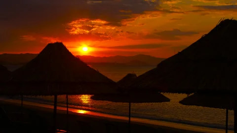 Sunset casting a warm glow behind colorful beach umbrellas Stock Footage 344313932