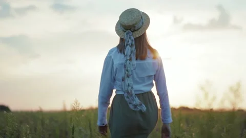 At sunset charming woman with hat walking turning look to camera on a field Stock Footage 138330837