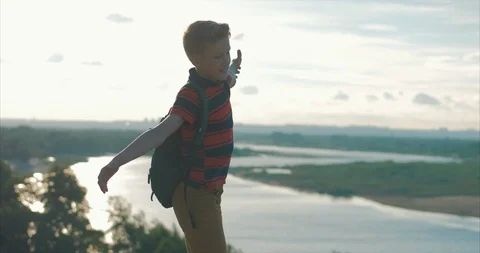 At Sunset Child in a Red Shirt a Backpack on His Back, Reaching to the Top on a Stock Footage 109380796