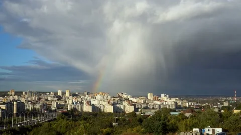 At sunset, a cloud runs over the city and it rains, and above the city rainbow Stock Footage 97403586
