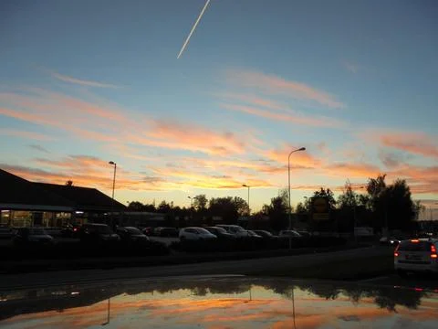 Sunset clouds and contrail over suburban parking lot with car roof reflection Stock Photos