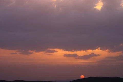A sunset with clouds and a orange sun setting in the sky. Stock Photos