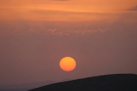 A sunset with clouds and a orange sun setting in the sky. Stock-Fotos