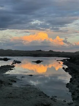 Sunset clouds reflected in still water on rugged terrain Stock Photos