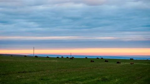 Sunset colored sky over green fields with with hay bales and utility poles Stock Photos