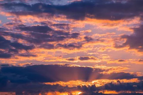 Sunset colorful clouds with sun rays emerging above horizon Stock Photos