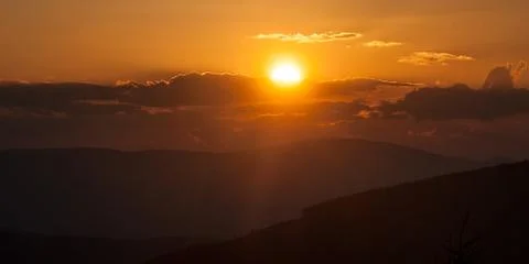 Sunset with colorful sky, sun, clouds and hills Stock Photos