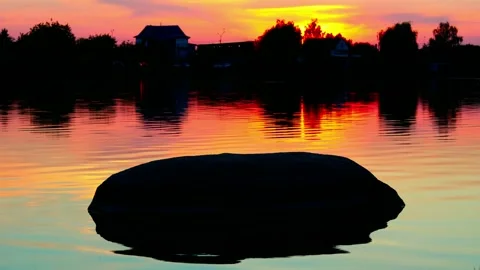 Sunset colors, lake, big stone in the water, small waves, silhouettes of trees Stock Footage 229424488