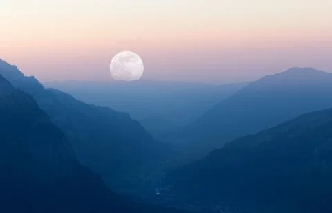 Sunset creating layered mountain landscape with moon at end of valley. Фото