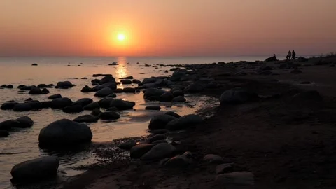 The sunset is dark. calm seashore with stones. dark silhouettes of people in the Stock Footage