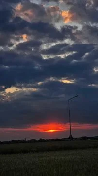 Sunset with dark clouds over a flat landscape and street lamp Stock Photos