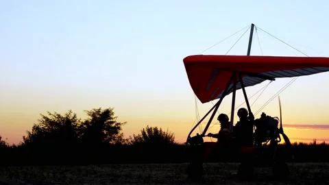 At sunset, dark silhouette of motorized hang glider with passenger and pilot 動画素材 137124153