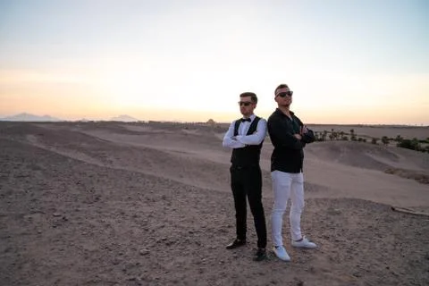 Sunset in the desert, two men in elegant clothes and sunglasses standing with Stock Photos
