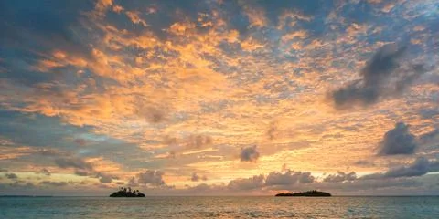 Sunset with dramatic clouds on the tropical beach. Panorama with two uninhabi Stock Photos