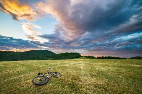 Sunset dramatic sky over meadow in Marche region, Italy. MTB lying on grass a Foto stock