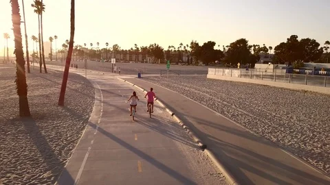 Sunset drone shot at the beach as two people ride off on bicycles Stock Footage 113513285