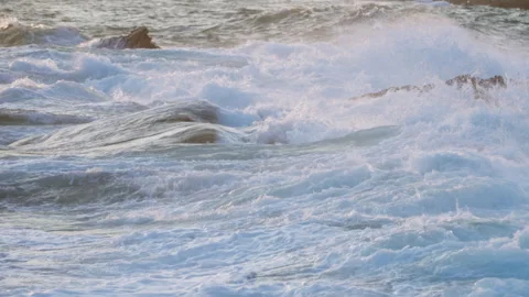 Sunset glistens on ocean, waves crash against jagged rocks, foam sprays. Coastal Stock Footage 272309952