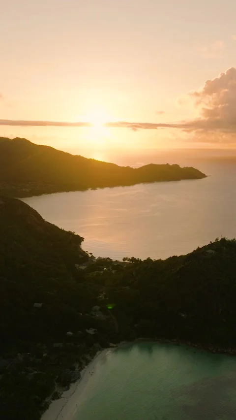 Sunset glow over lush green hills and calm ocean waters. Praslin, Seychelles. Stock Footage 311607150