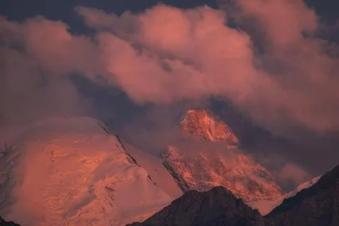 Sunset glow on the snow-covered summit of Khan Tengri Peak framed by pink clo Stock Photos